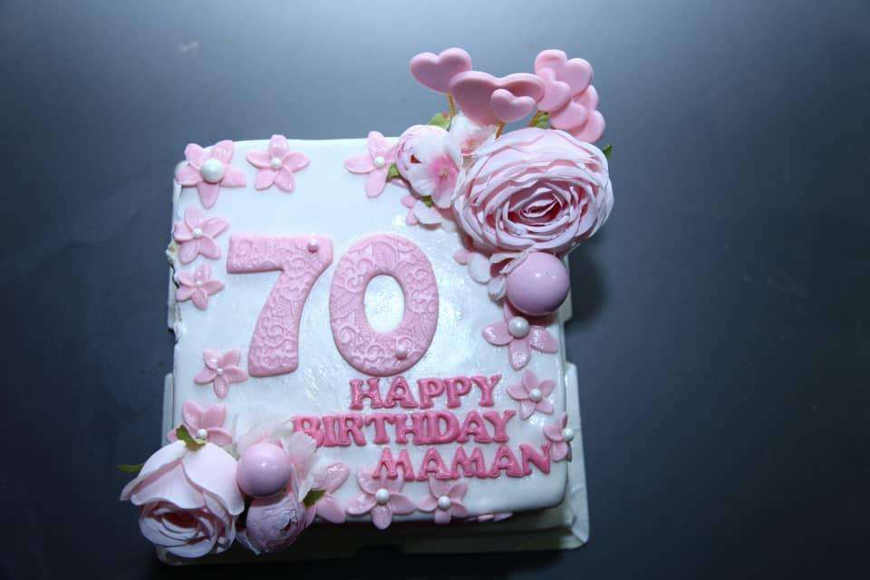Photo du gateau d'anniversaire de ma mère. Le gateau est carré sur un fond blanc avec des fleurs roses avec le texte suivant:"70 Happy Birthday maman"